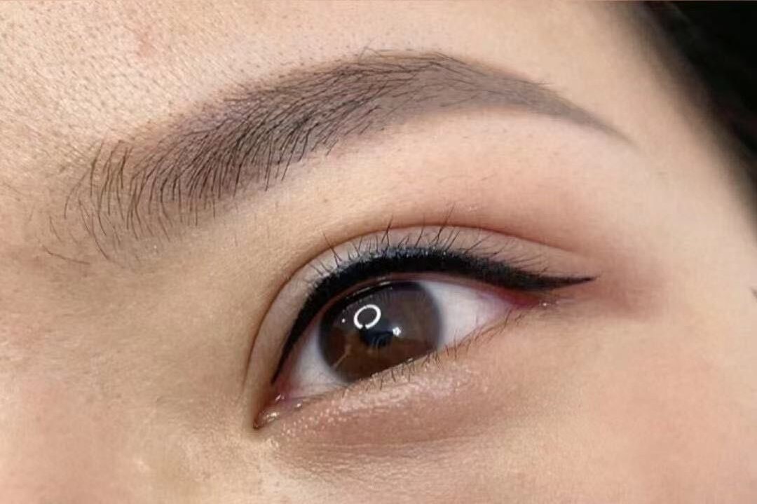 A client's open eye in close up: a dark line worked along the upper lash line, thickening toward the outer corner and lifting into a short wing past it.